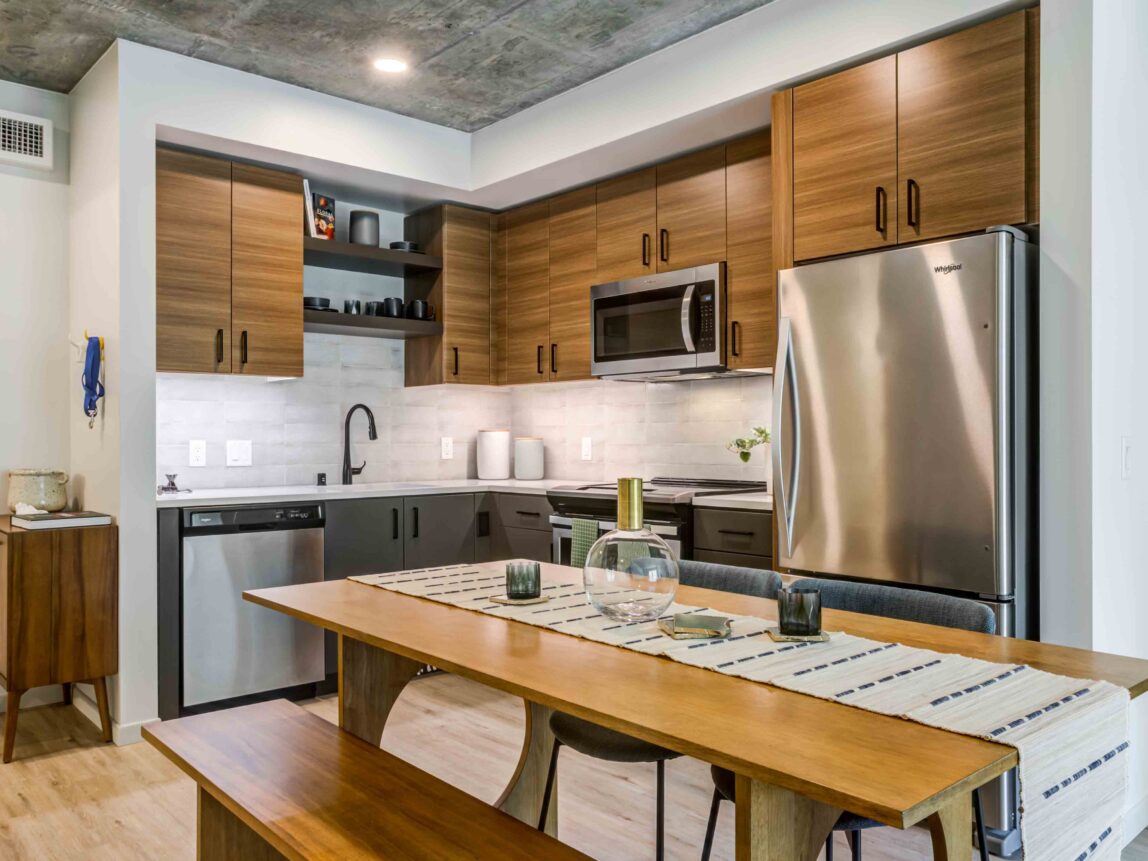 One-Bedroom Luxury Apartments in Downtown San Francisco, CA - 50 Jones - Kitchen with Luxury Wood-Style Vinyl Plank Flooring, Exposed Concrete Ceiling, Stainless-Steel Appliances, Caeserstone Quartz Countertops, Wood-Tone Cabinetry, and Picnic-Style Table with Bench and Chairs.