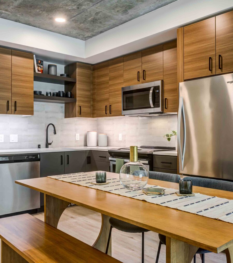 One-Bedroom Luxury Apartments in Downtown San Francisco, CA - 50 Jones - Kitchen with Luxury Wood-Style Vinyl Plank Flooring, Exposed Concrete Ceiling, Stainless-Steel Appliances, Caeserstone Quartz Countertops, Wood-Tone Cabinetry, and Picnic-Style Table with Bench and Chairs.
